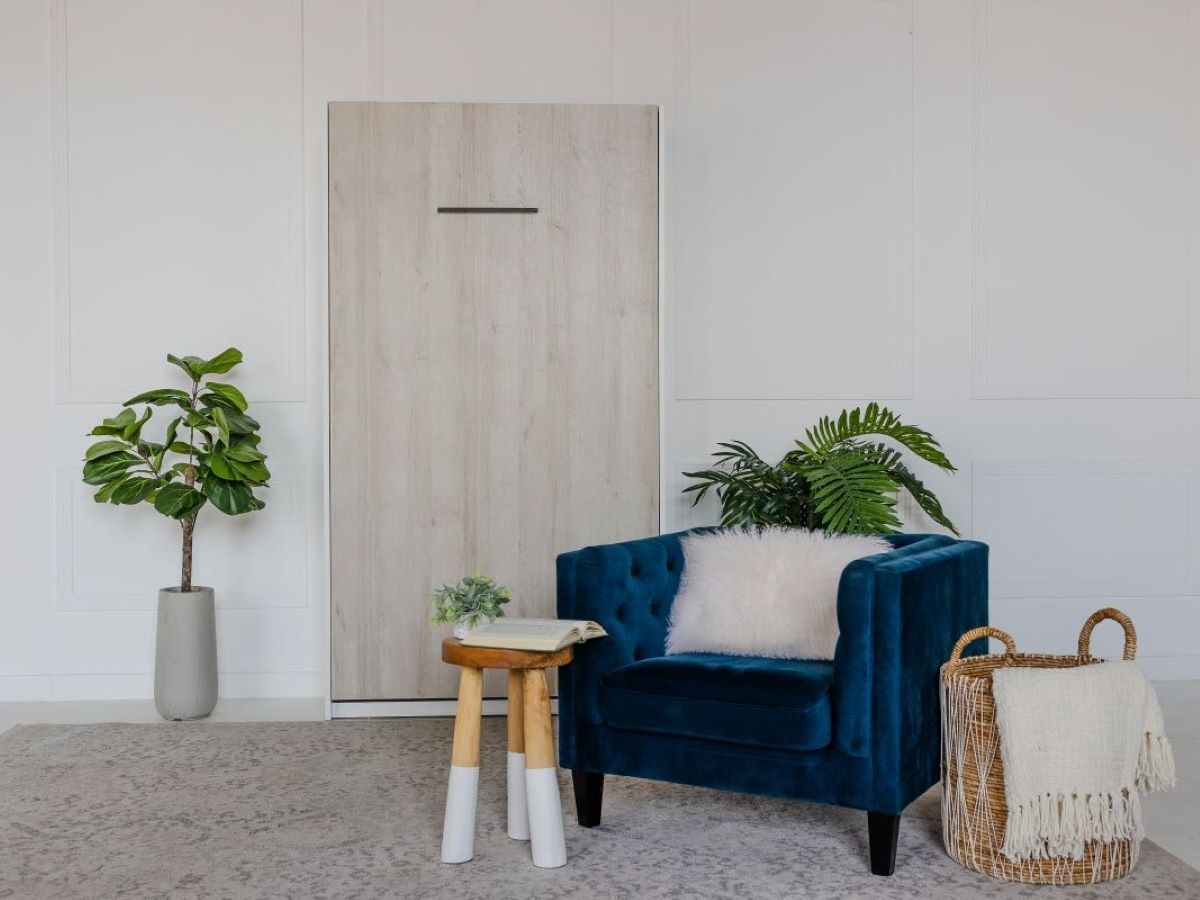 staged image of vertical tilt single/twin melamine murphy wall bed in studio with lounge chair and plants/decor